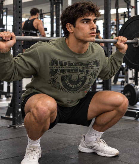 Man performing a barbell squat in a gym, wearing a military green GYMSTAR Blood, Sweat and Iron crewneck sweatshirt.