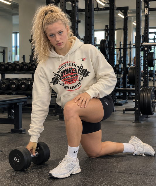 Emelie Johansson kneeling beside a dumbbell in a gym, wearing a sand-colored GYMSTAR BRUTALIKA pullover hoodie with a red and black graphic.