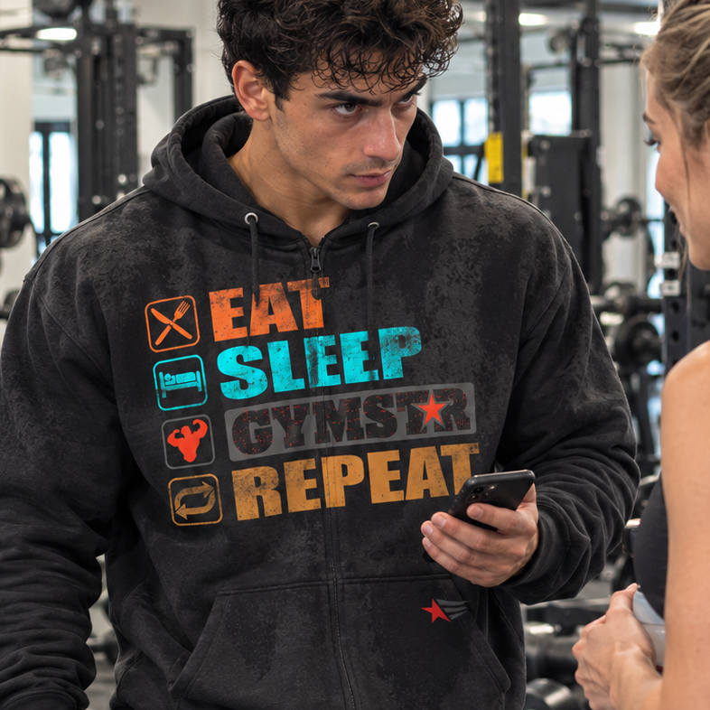 Luca Moretti wearing a black GYMSTAR Eat Sleep Repeat full-zip hoodie, holding a smartphone and workout towel while talking to a woman in a gym.