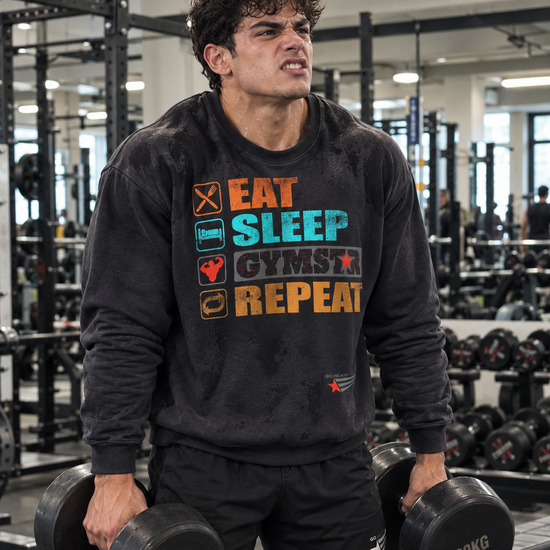 Luca Moretti wearing a black GYMSTAR Eat Sleep Repeat crewneck sweatshirt with colorful graphic print and sweat marks, performing dumbbell shrugs during a gym workout.