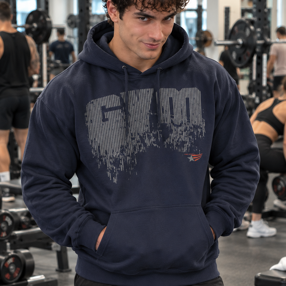 Luca Moretti wearing a navy blue GYMSTAR pullover hoodie with a distressed GYM graphic, smiling at the camera with his hands in the front pocket while other athletes train in the background.