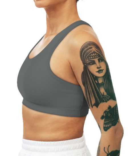 
A women's solid gray athletic sports bra Gymsatr, shown from the side. It has a scoop neckline and a racerback style. The sports bra is worn by a person with tattoos on their upper arm.