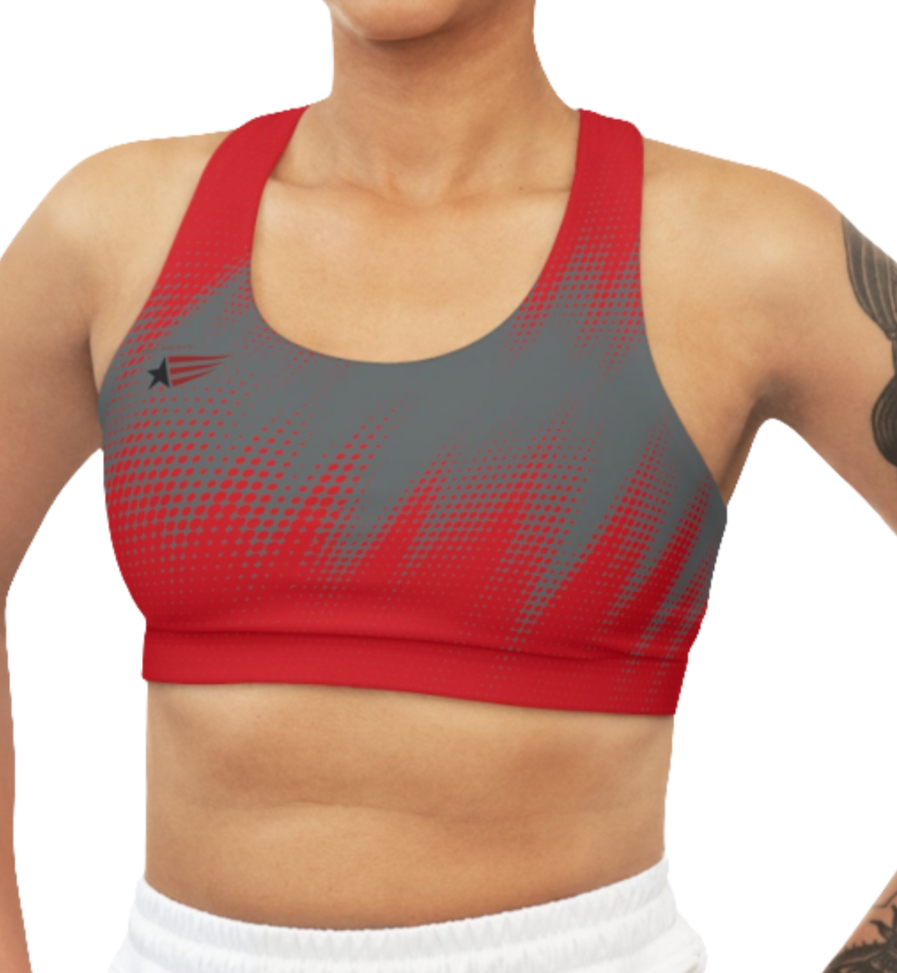 A woman wearing athletic sports bra, shown from the front. The main body is gray with a red, dotted, gradient pattern that radiates from the sides and bottom. The straps are solid red and form a racerback style at the back. A small logo featuring a star and three red and blue stripes is on the left side of the chest.