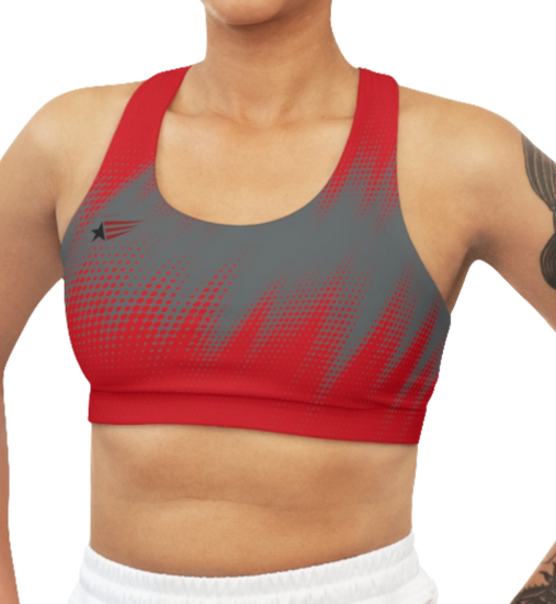 A woman wearing athletic sports bra, shown from the front. The main body is gray with a red, dotted, gradient pattern that radiates from the sides and bottom. The straps are solid red and form a racerback style at the back. A small logo featuring a star and three red and blue stripes is on the left side of the chest.