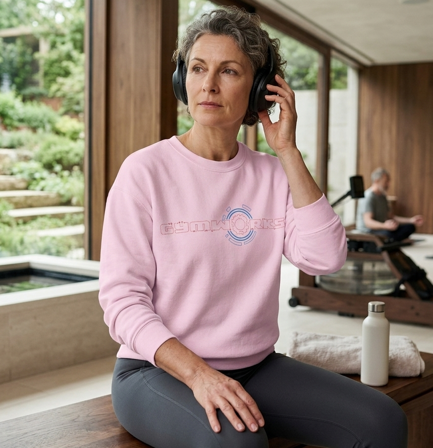 Woman in pink Gymworks sweatshirt with headphones, sitting indoors with a garden view.