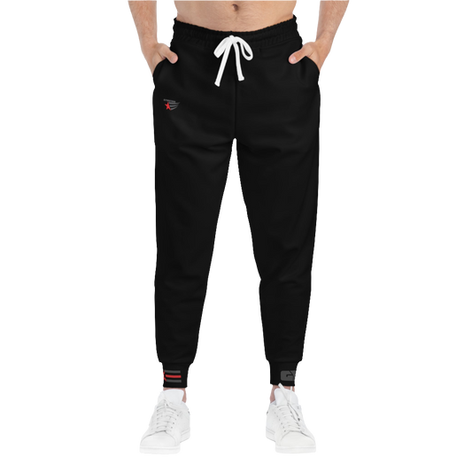 A person standing frontal, wearing black joggers Gymstar with a logoand white sneakers. The joggers have a ribbed bottom and waistband cuffs, and feature two side pockets.