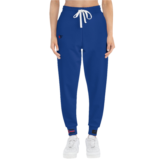 A woman wearing blue sports joggers with an elastic waistband and drawstrings, featuring a logo on the left leg and a white sneaker front side view.