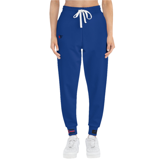 A woman wearing blue sports joggers with an elastic waistband and drawstrings, featuring a logo on the left leg and a white sneaker front side view.