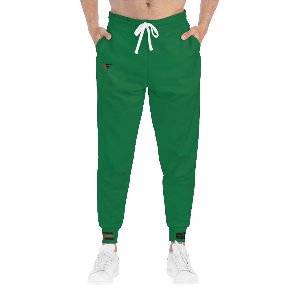 A person wearing green sports joggers with an elastic waistband and drawstrings, featuring a logo on the left leg and a white sneaker.