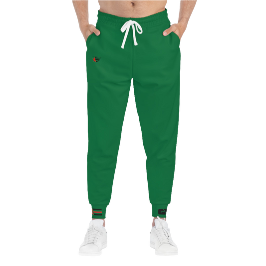 A person wearing green sports joggers with an elastic waistband and drawstrings, featuring a logo on the left leg and a white sneaker.