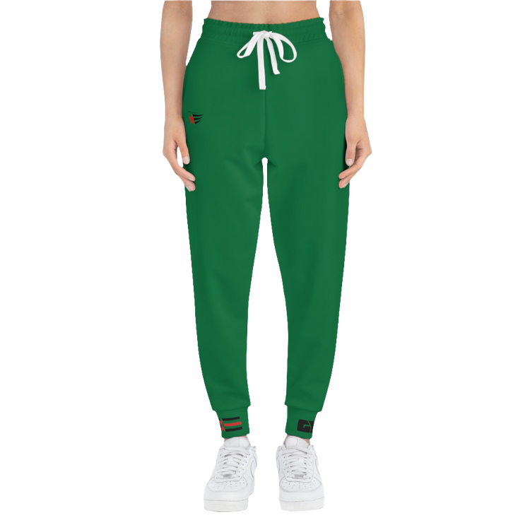A woman wearing green sports joggers with an elastic waistband and drawstrings, featuring a logo on the left leg and a white sneaker.
